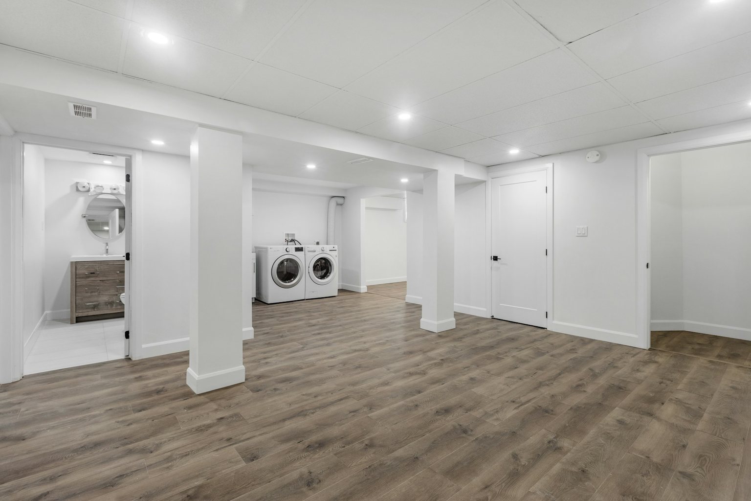 Finished basement with boxed columns, a drop ceiling and wood-look flooring