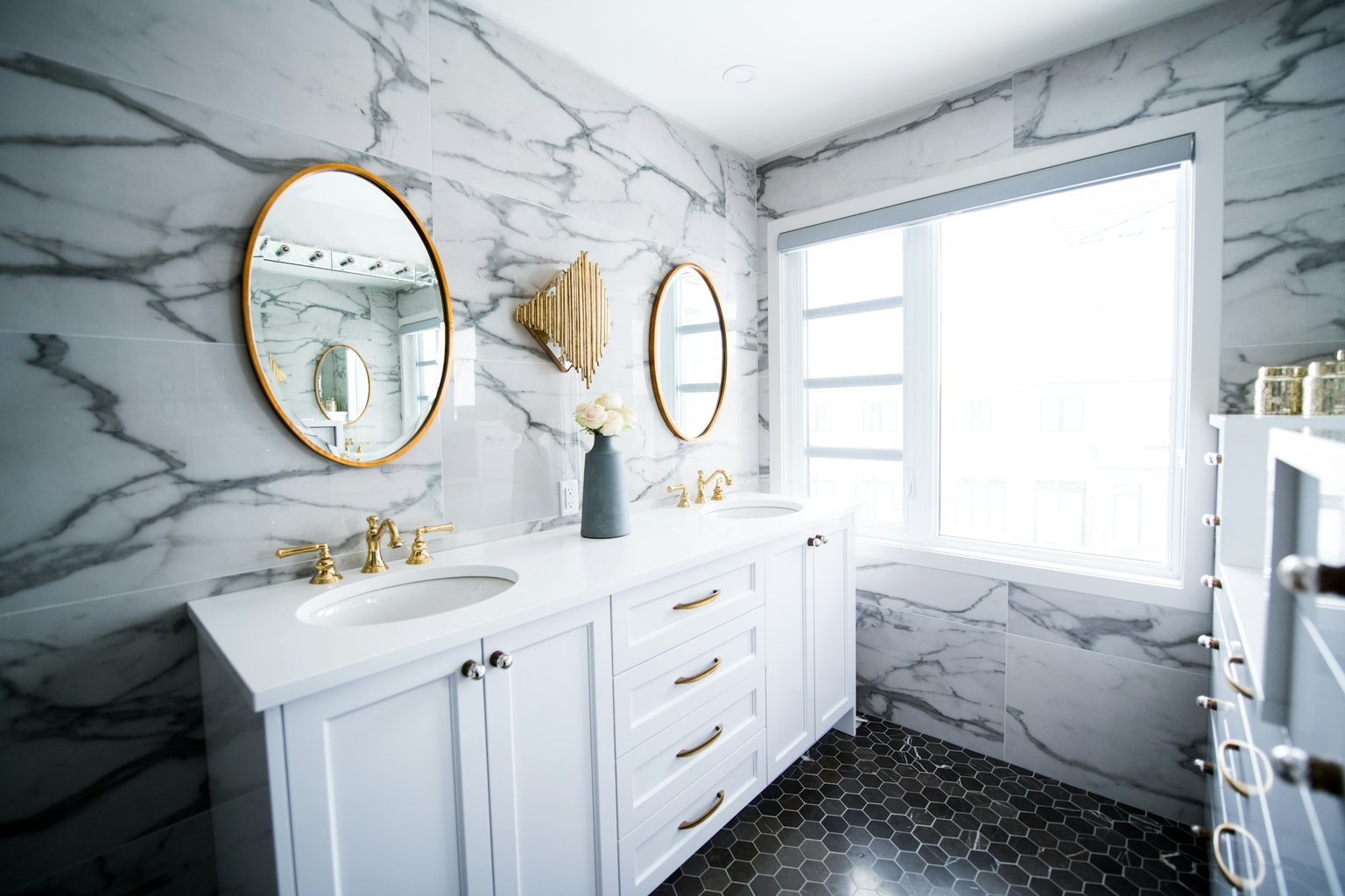 Remodeled bathroom with a double vanity, round mirrors and hexagonal floor tiles