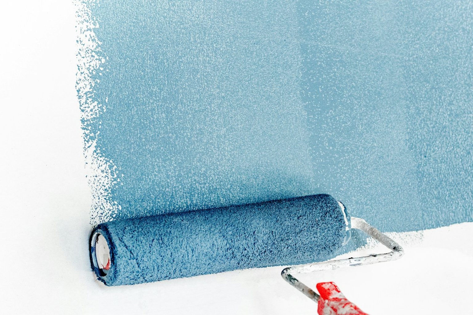 Paint roller applying blue paint to a white wall