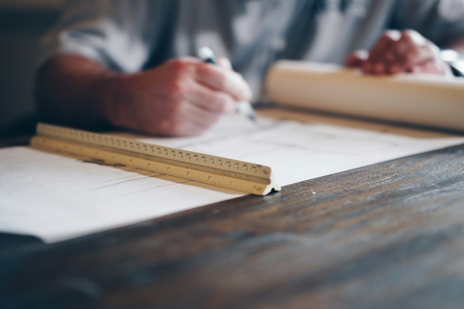 Hands drawing project plans with a scale ruler and rolled drawings
