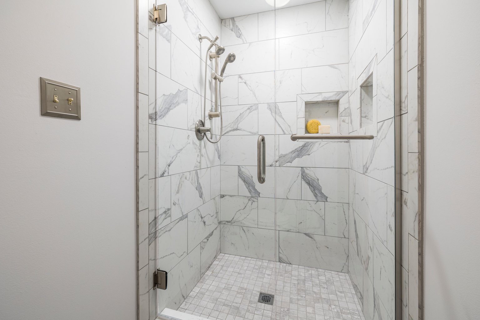 Glass-enclosed shower with marble-look wall tiles and a mosaic tile floor