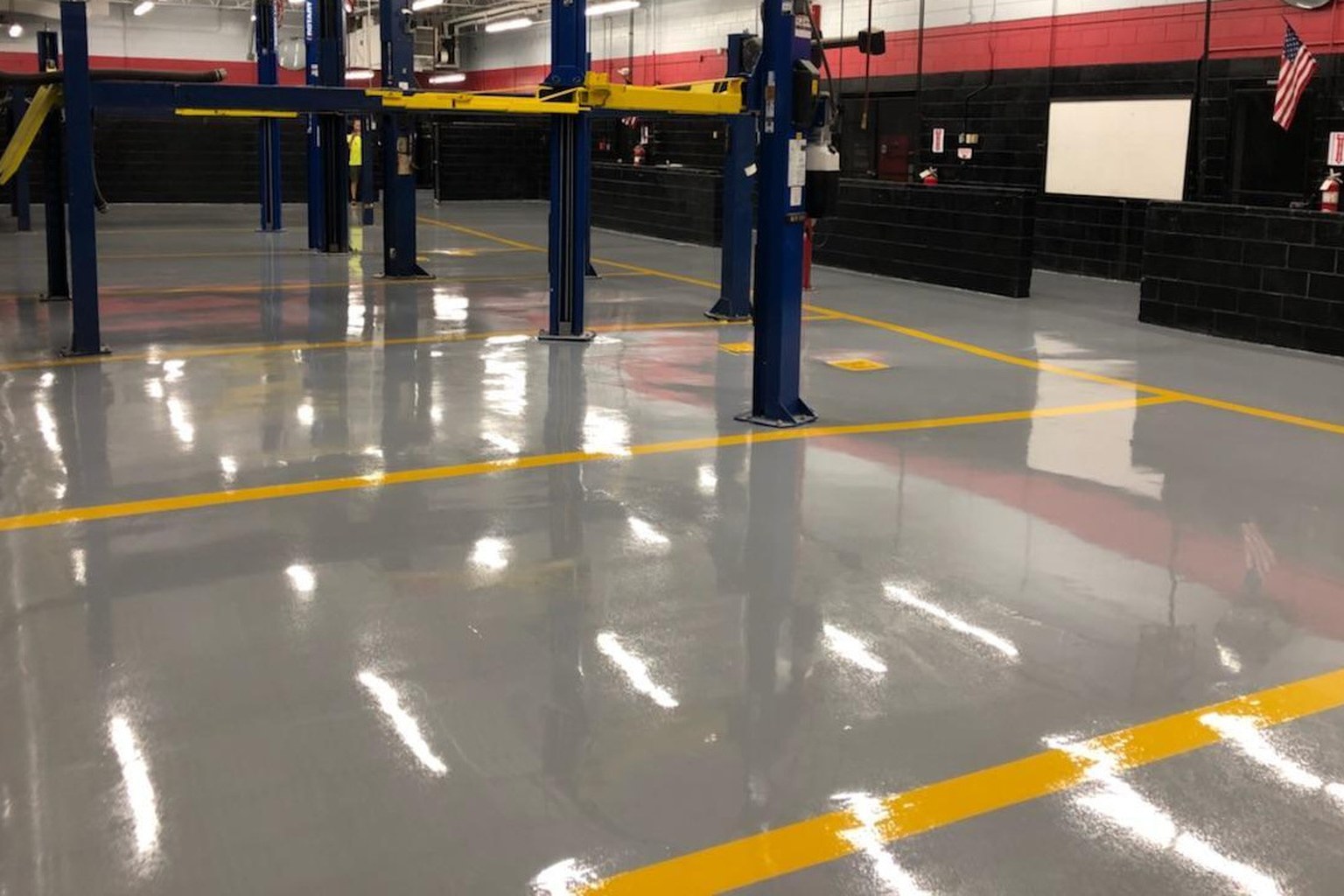 Glossy gray coated automotive service floor with yellow bay markings and blue vehicle lifts.