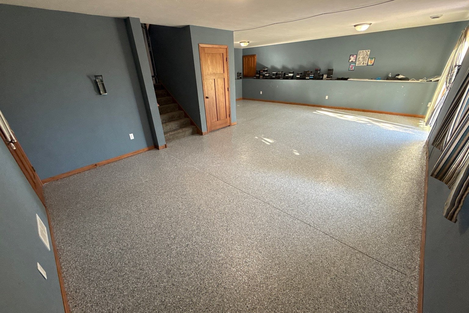Finished basement with blue-gray walls, an interior staircase, and a continuous gray decorative flake floor.