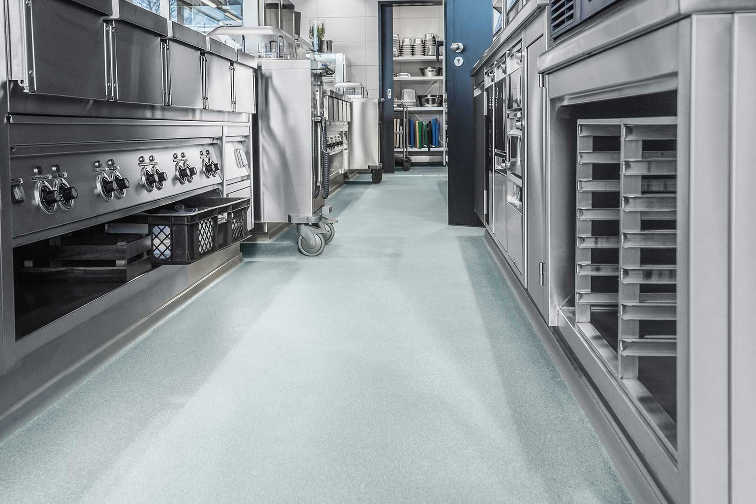 Seamless pale blue resin floor between stainless steel commercial kitchen appliances.