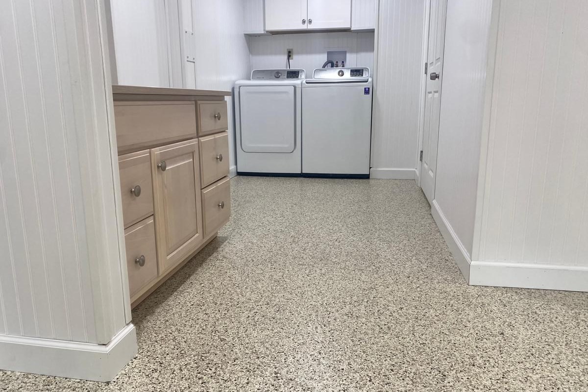 Laundry room with a light flake epoxy floor, white washer and dryer, and wood cabinets.