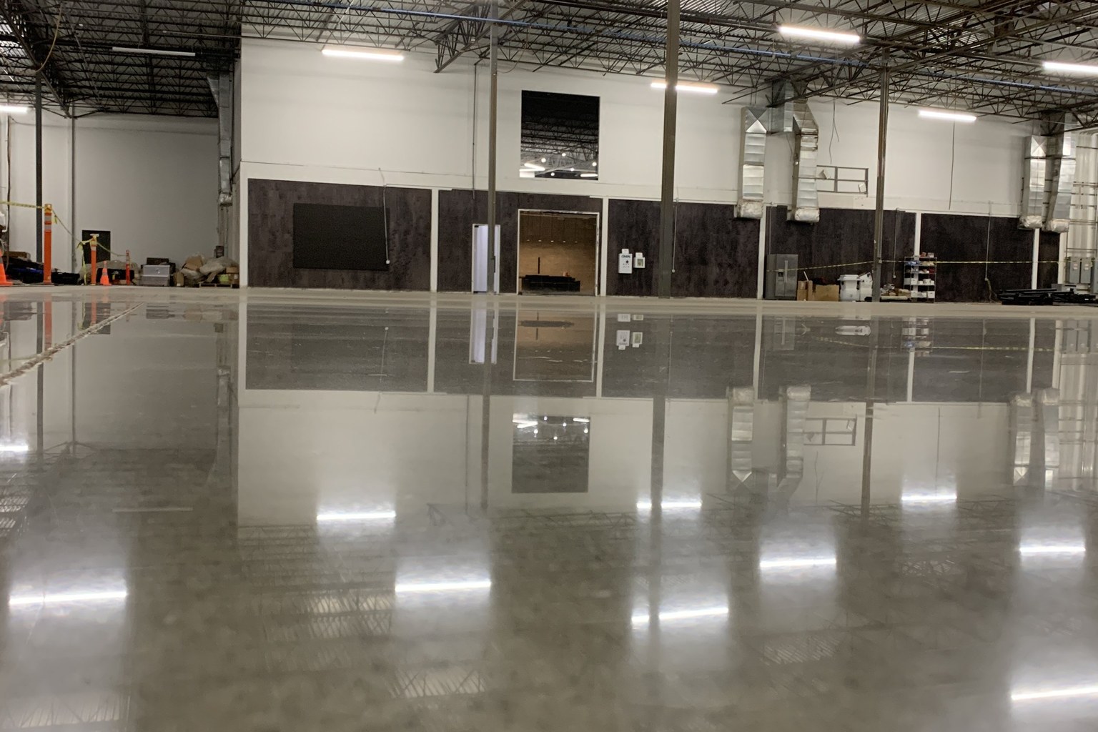 Polished concrete warehouse floor reflecting overhead lights and the building structure.