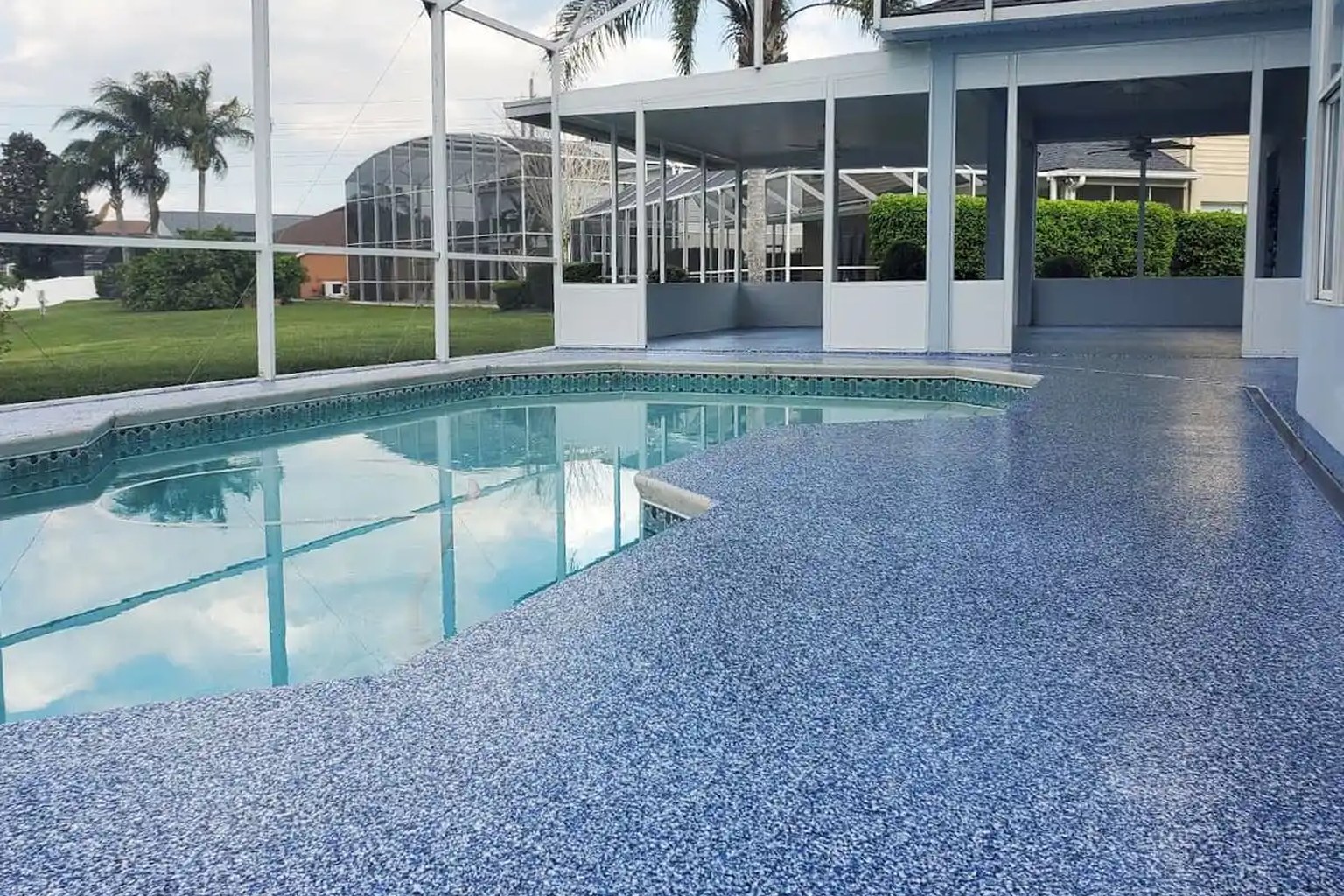 Swimming pool surrounded by a blue decorative flake deck inside a screened residential enclosure.